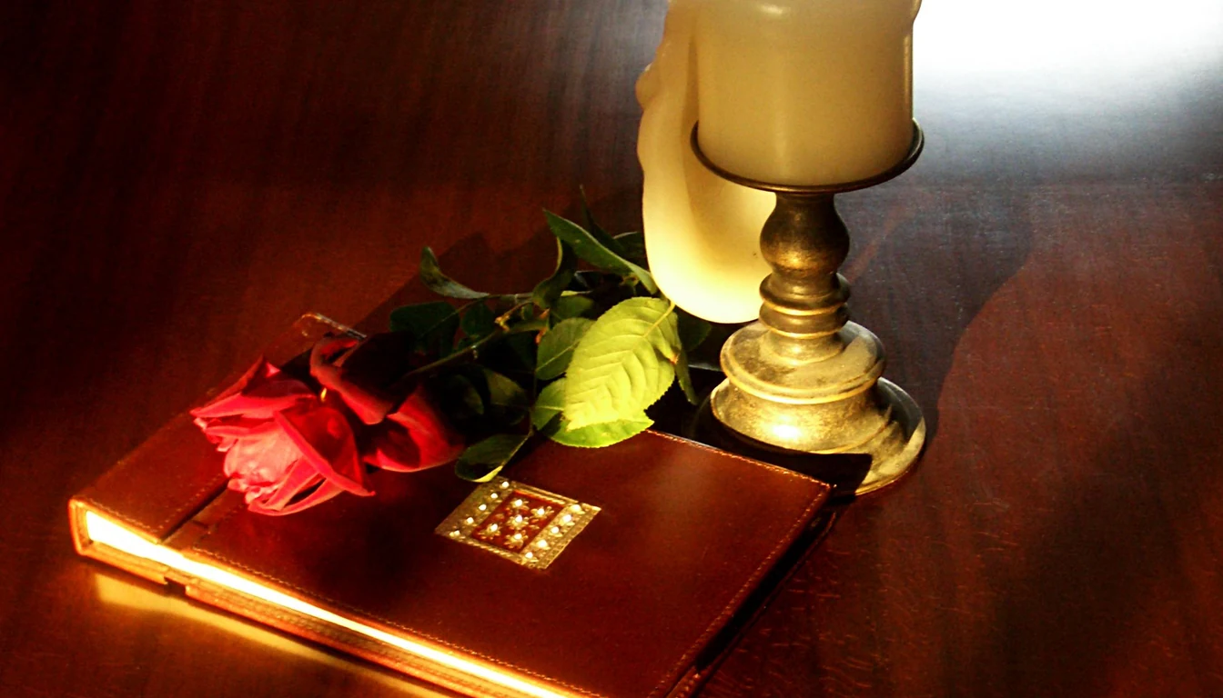 A leather-bound photograph album beside a candle and a rose on polished wood