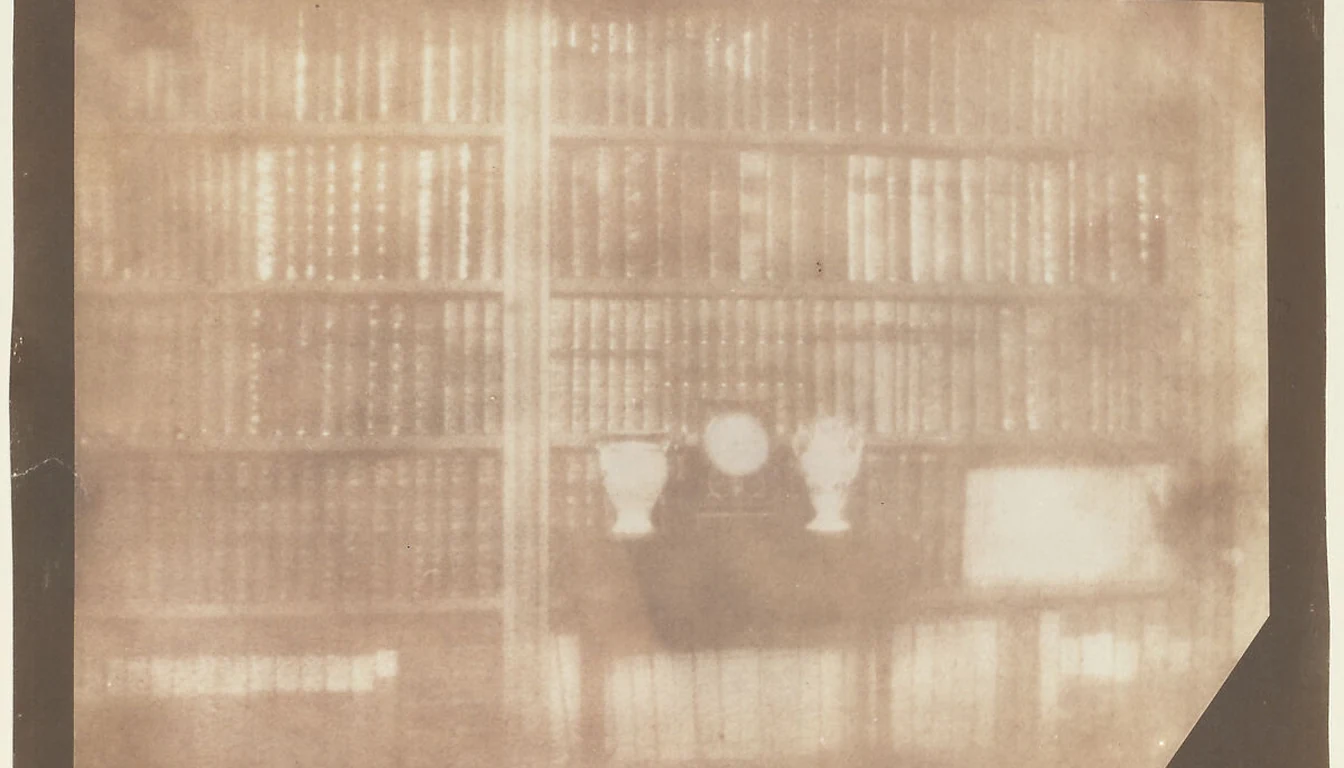 A softly faded nineteenth-century photograph of rows of clothbound books, two vases and a small clock in a bookcase